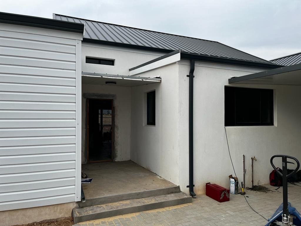 Corner of a finished house showing standing-seam roof and steel wall cladding under an overcast sky