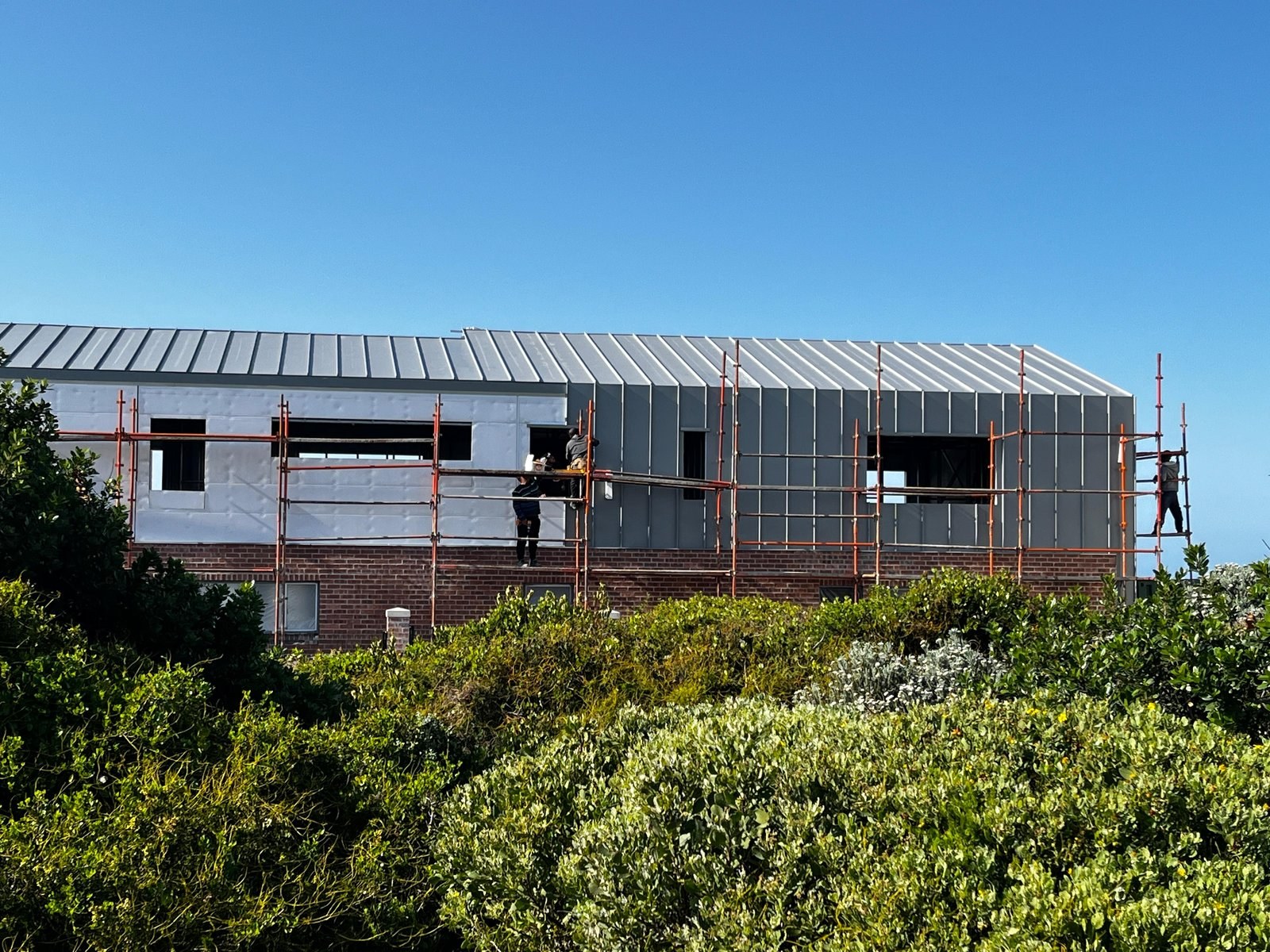 Workers on scaffolding fixing steel wall cladding panels to a coastal house