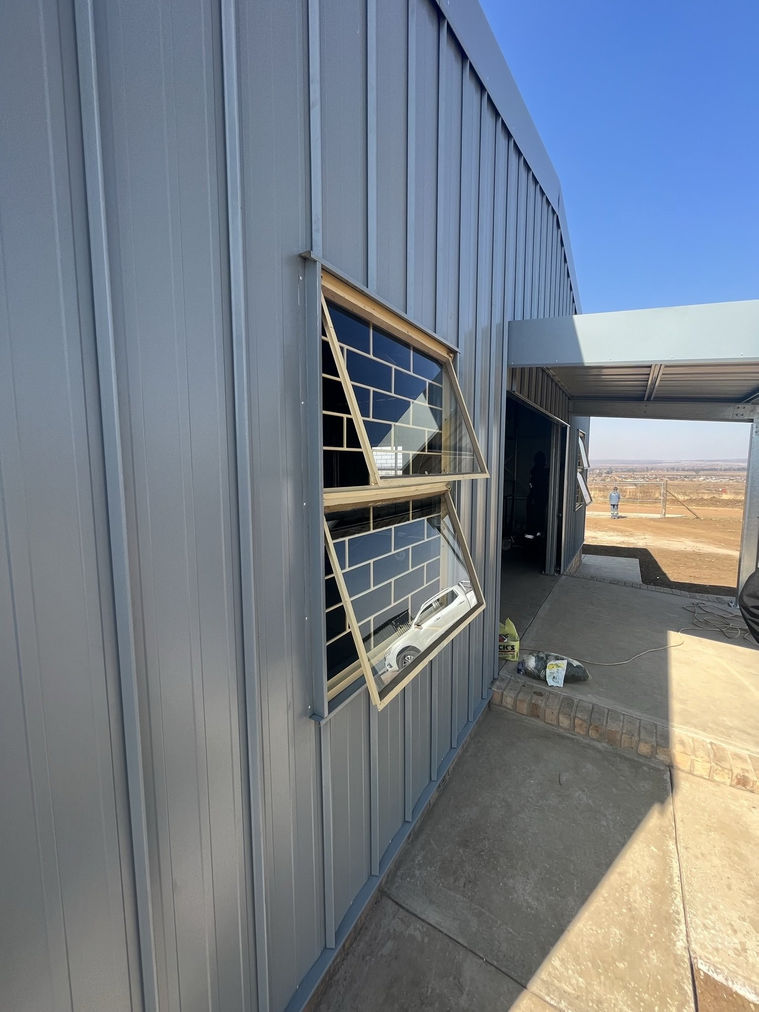 Open awning window in a steel-clad wall, viewed alongside an open bay door