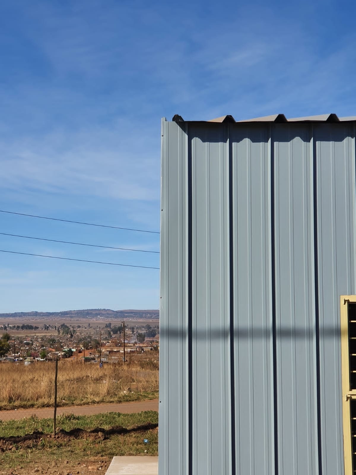 Close-up of vertical steel wall cladding at a building corner overlooking a township in the distance