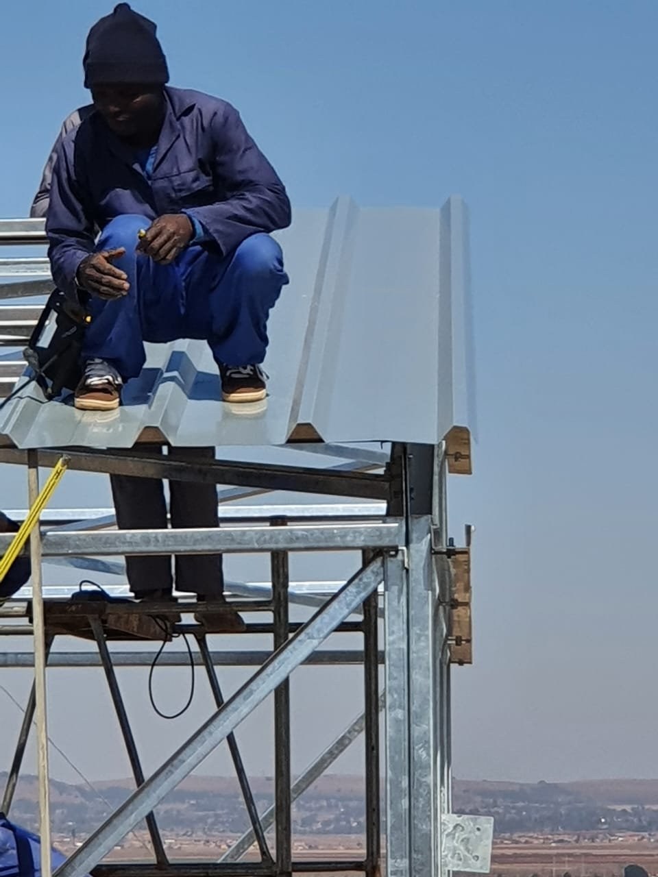 Worker fitting roof sheeting while seated on a scaffold tower