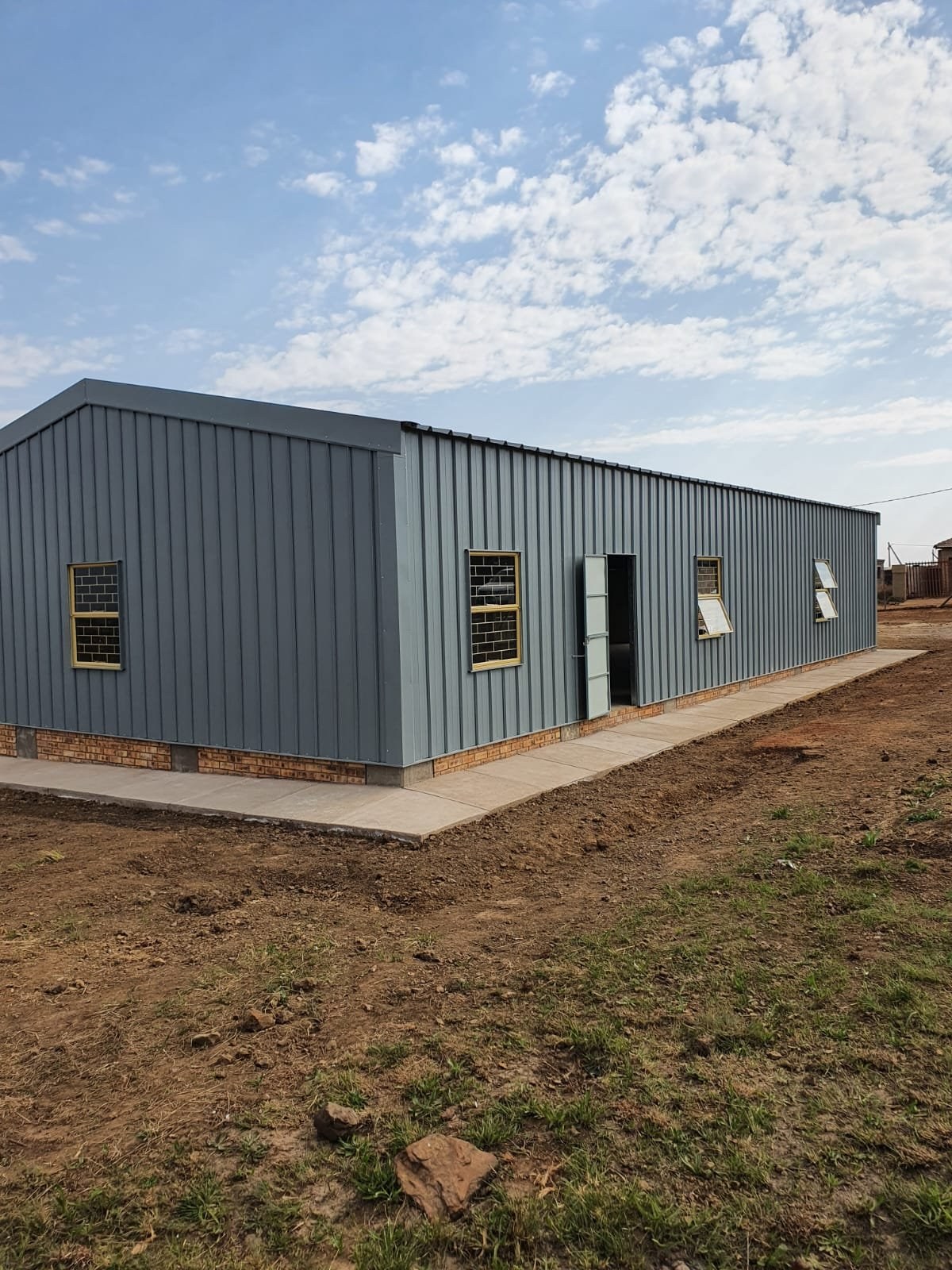 Three-quarter view of a steel-clad building corner showing door, windows and brick base course