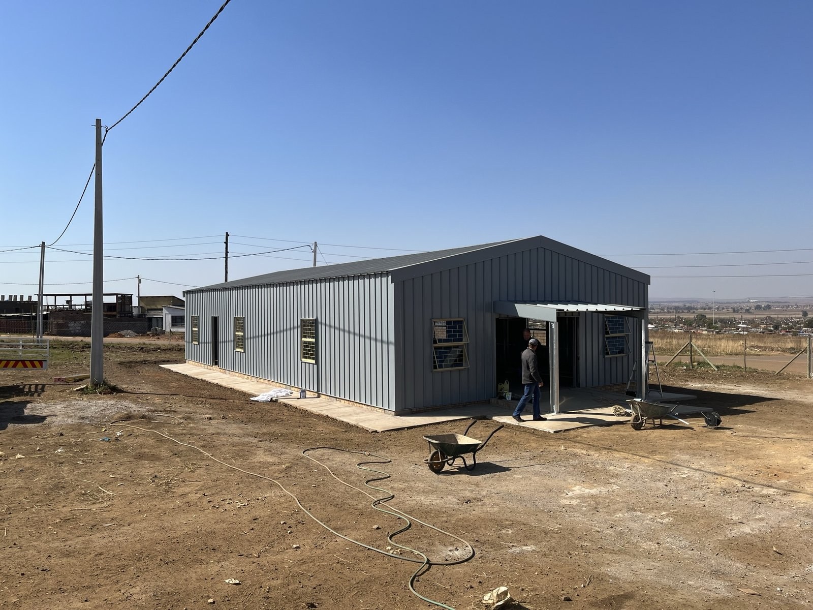 Worker walking into a steel-clad warehouse through an open bay door, hose reels on the ground outside