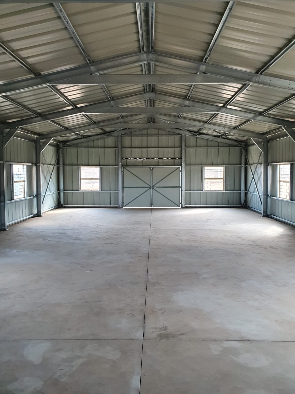 Empty warehouse interior showing exposed steel roof trusses and a closed double door at the gable end