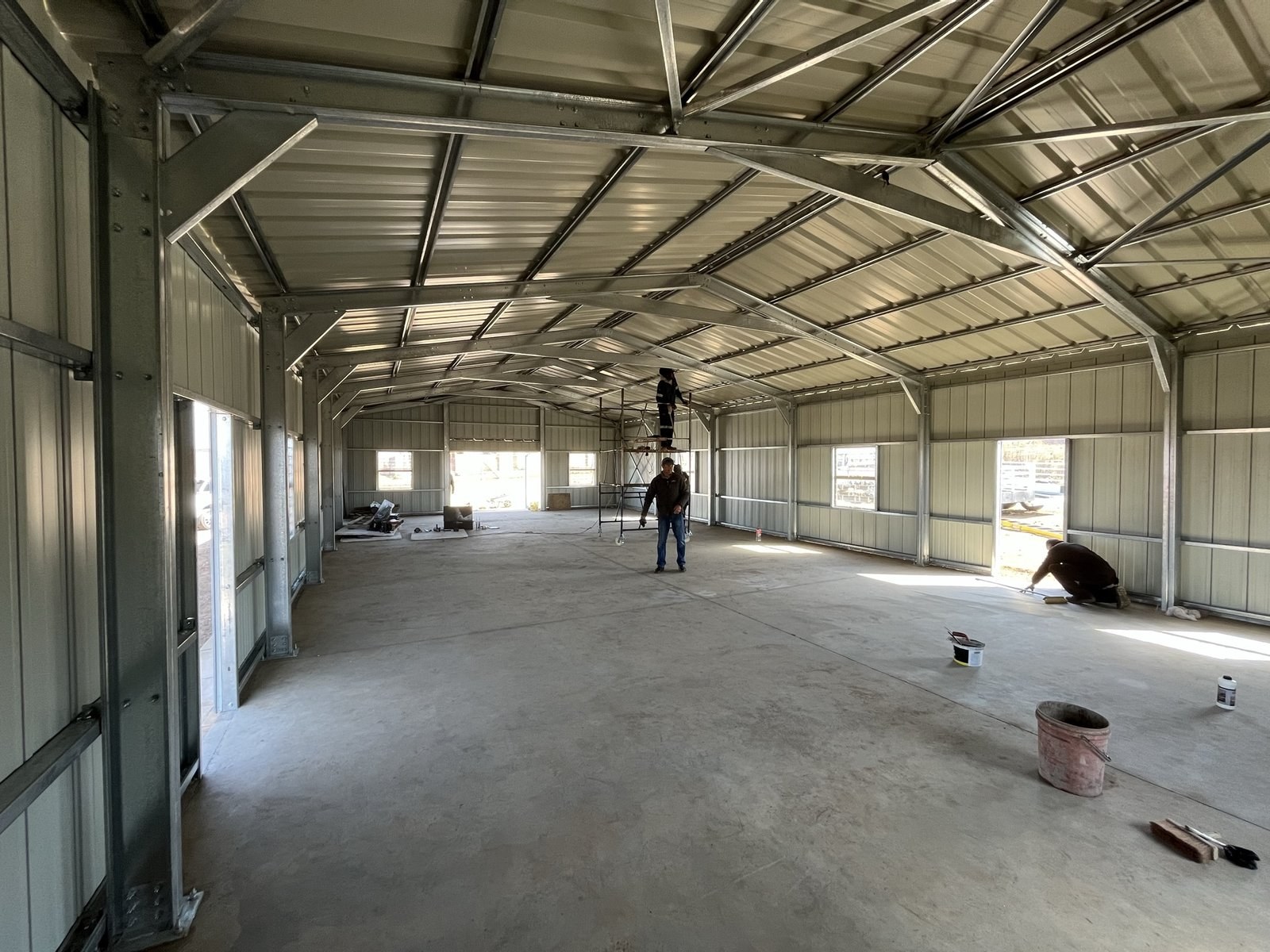 Workers finishing the floor and steelwork inside a steel-clad warehouse under construction