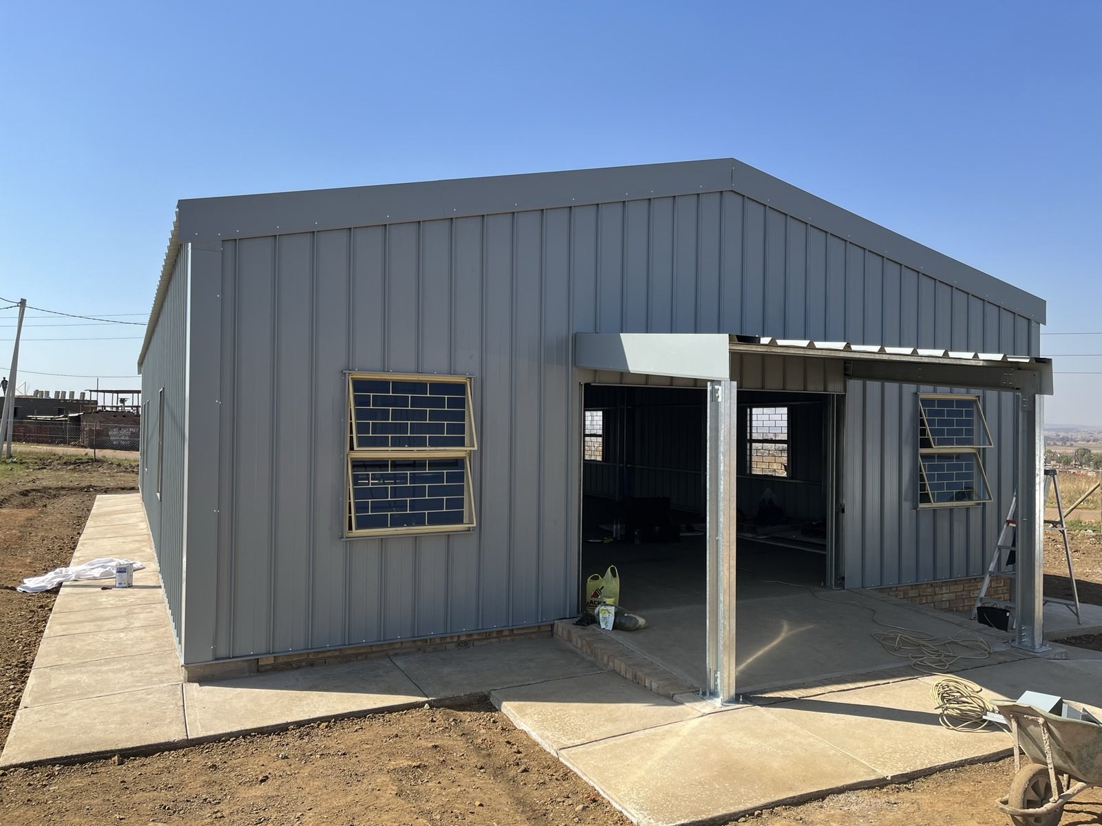 Corner view of a steel-clad building with an open bay/carport opening and window either side