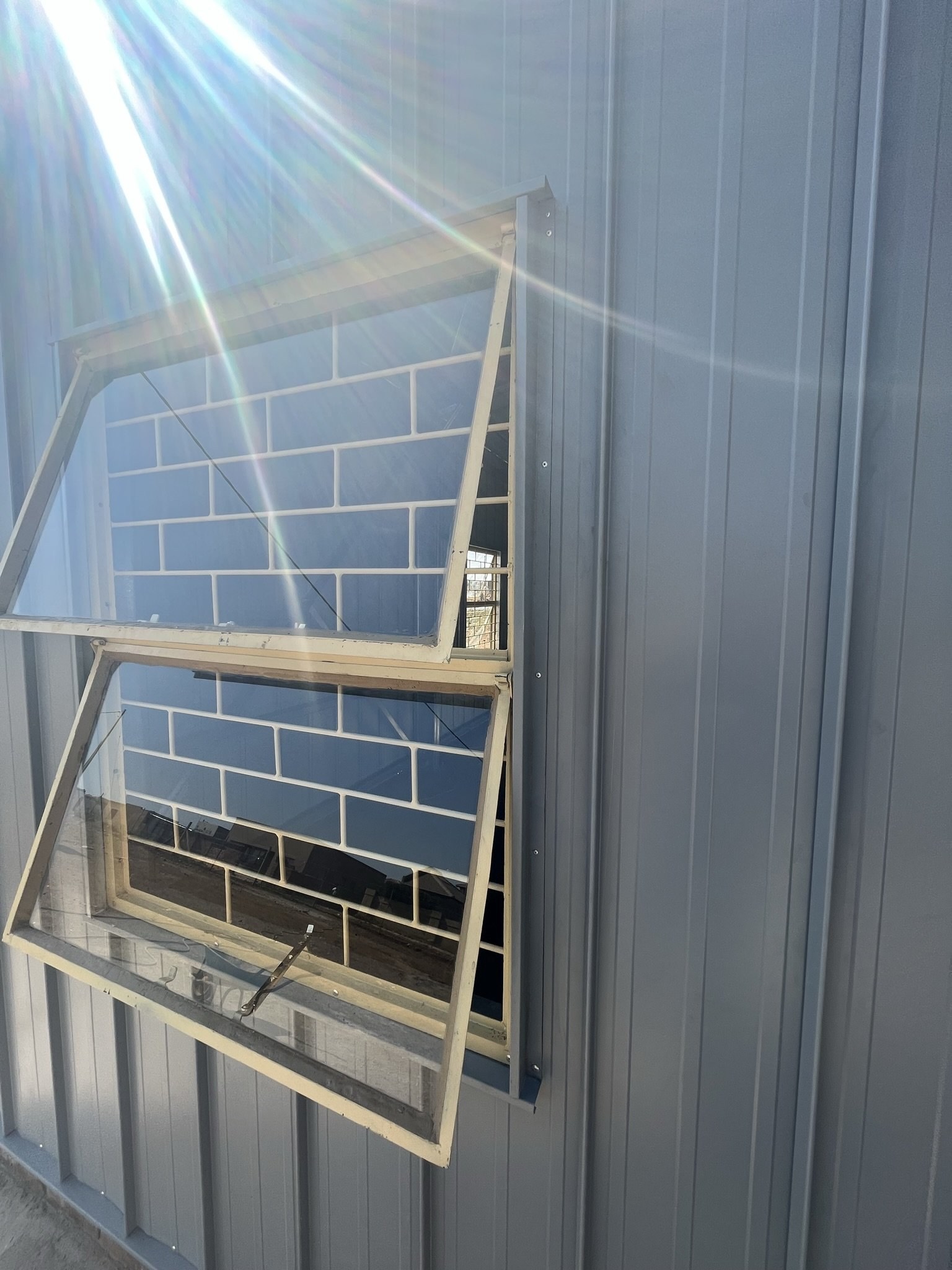 Close-up of an open awning window with brick-pattern burglar bars set into a steel-clad wall