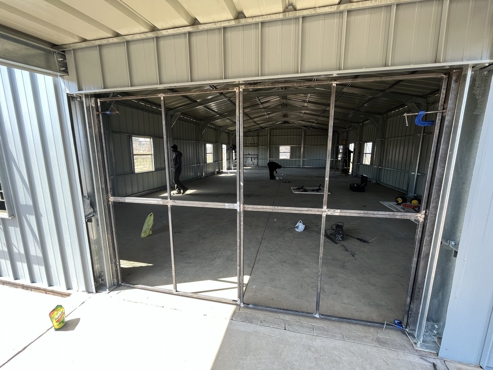 Interior view through open bay doors showing steel wall framing and window openings mid-installation