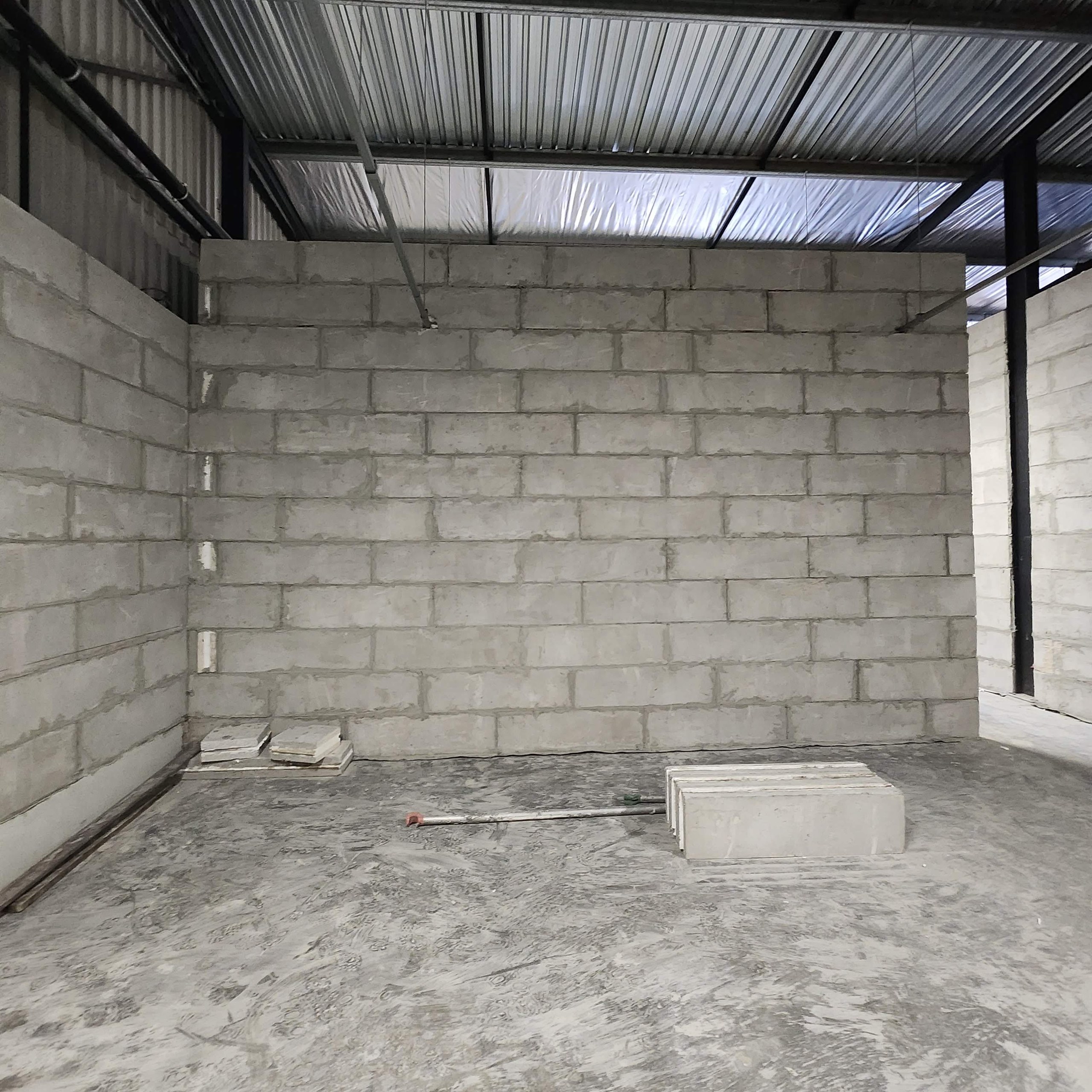 Internal walls laid course by course in stretcher bond from large lightweight blocks inside a steel-framed building, with spare units stacked on the floor and the mortar joints still exposed before plaster.