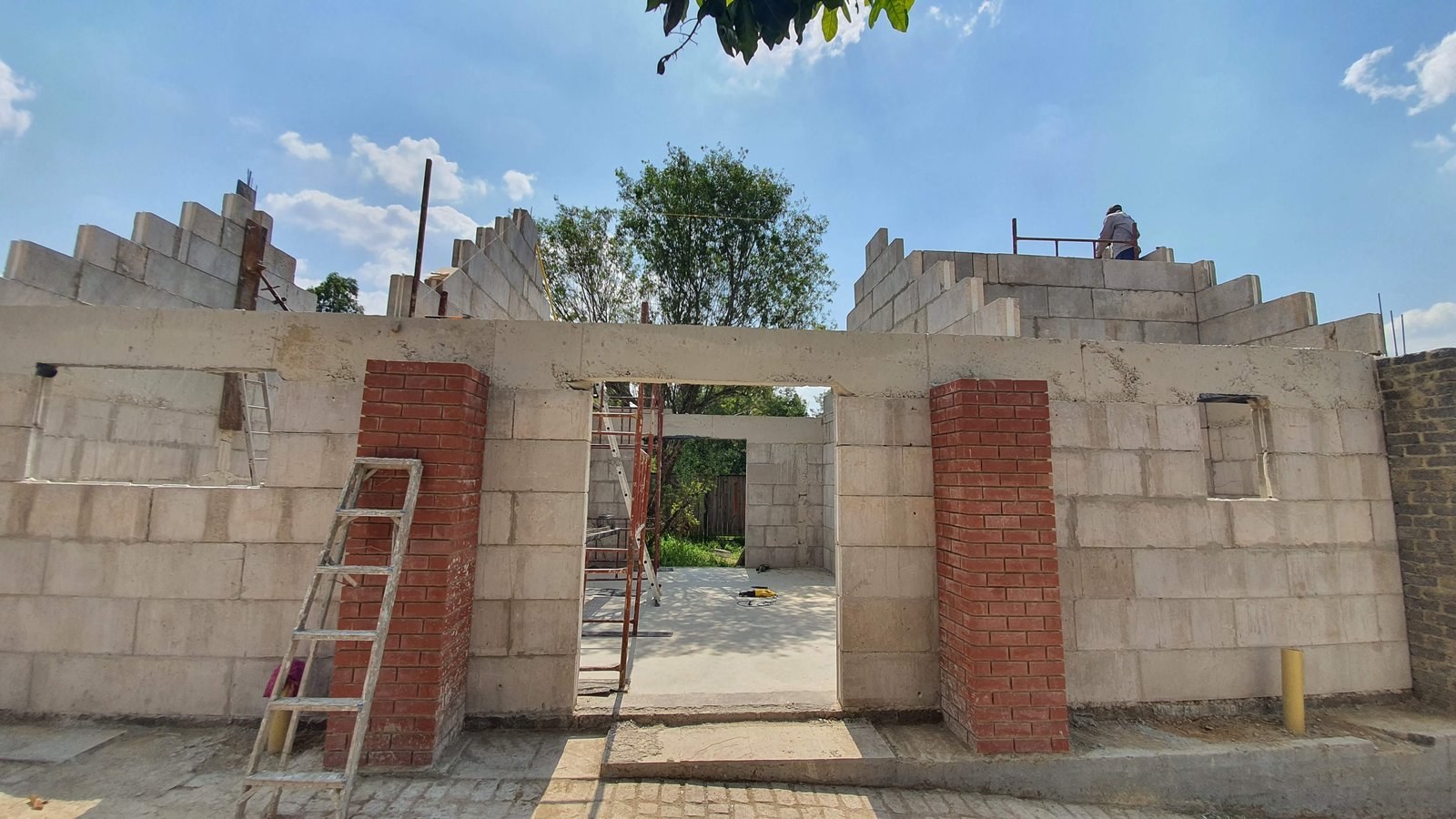 Walls going up in stretcher bond from large lightweight blocks, with a concrete lintel over the opening and clay face-brick piers alongside. Shown before plastering.