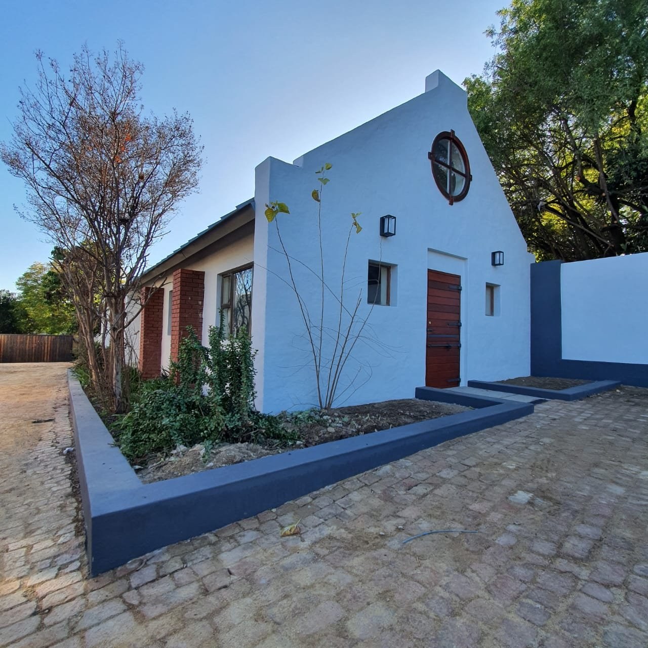 Completed home exterior at dusk, plastered gable end with round window and face-brick piers.