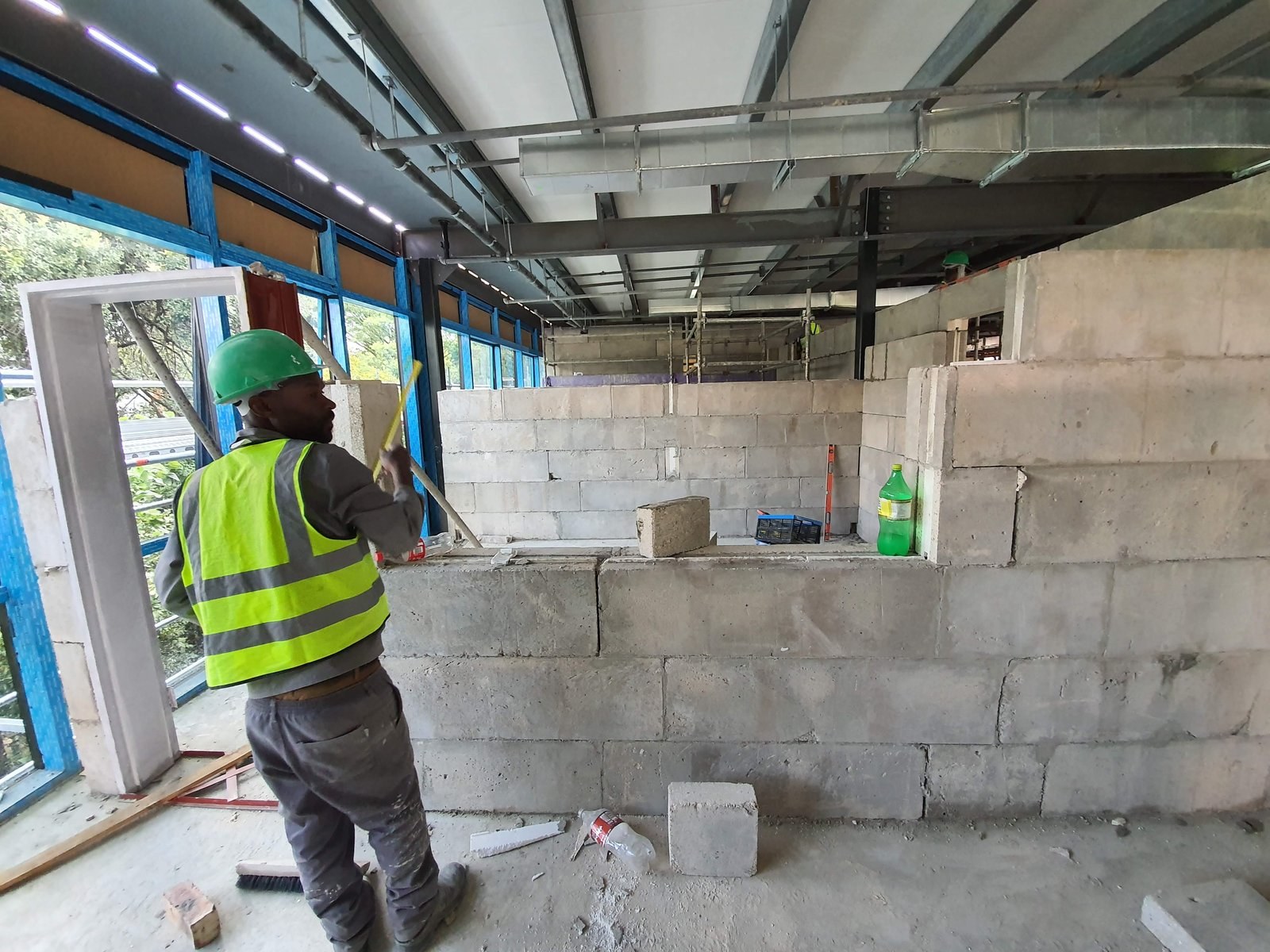 Worker checks level on a block wall being built inside a steel-frame commercial building shell.