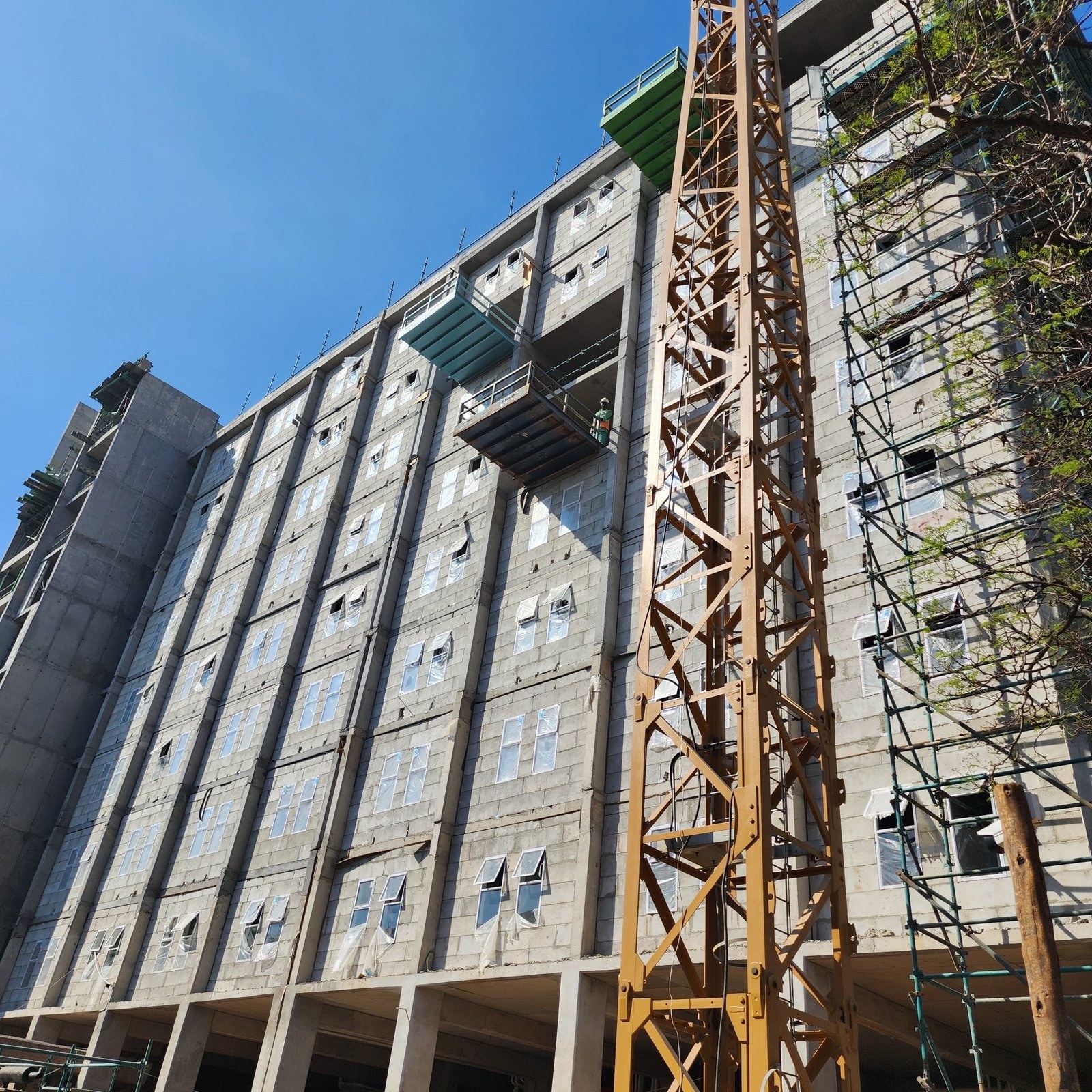 Multi-storey block building under construction, tower crane and hoist platform against the facade.