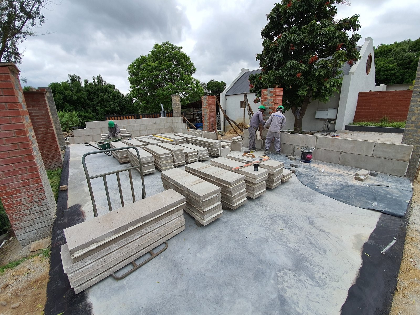 Stacked panels and brick piers on a garden-wall site, with workers building a low wall.