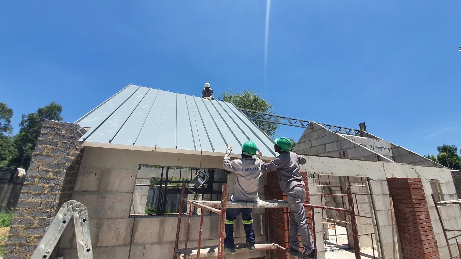 Timber roof trusses being fitted over block gable walls, house shell exterior.