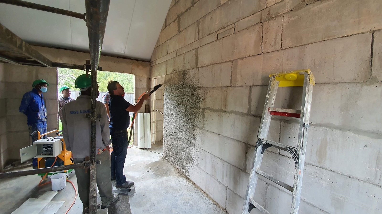 Machine-sprayed plaster being applied to a bare block wall inside a vaulted room.
