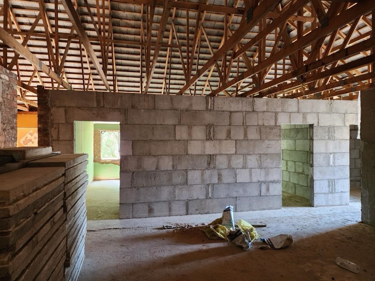 Interior under timber roof trusses, with block partition walls and stacked brick piers.