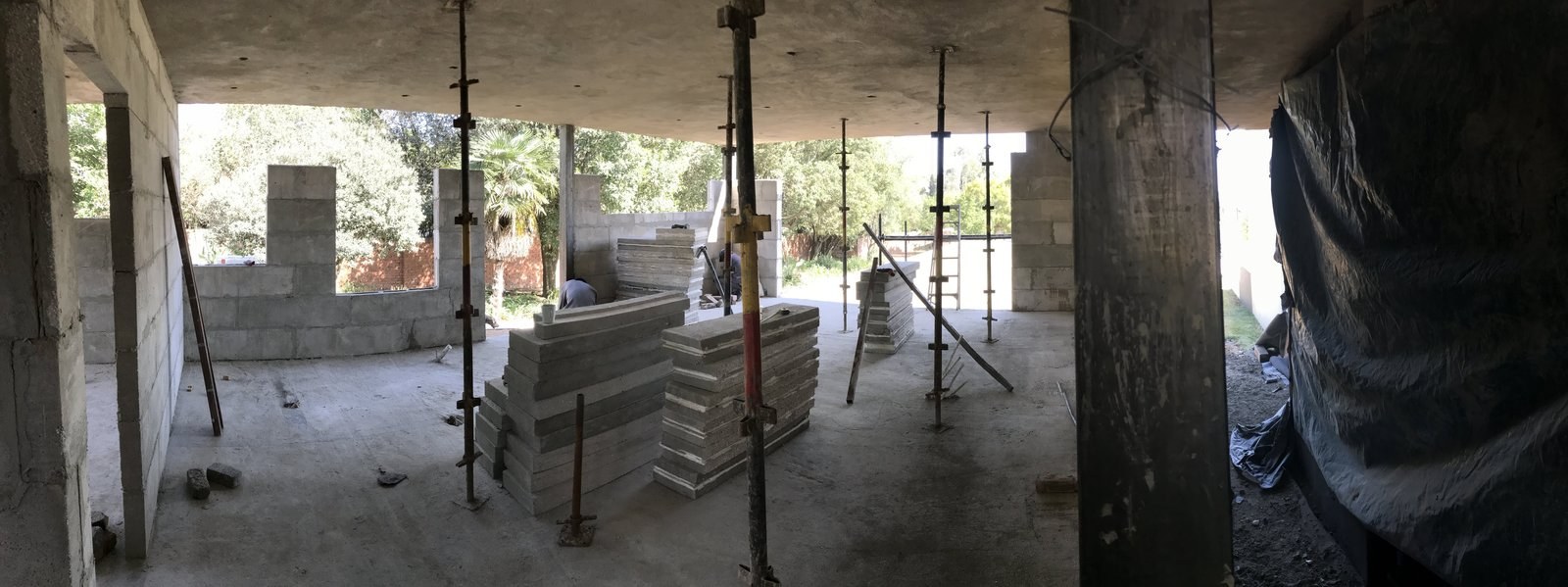 Panels stacked on site under a concrete slab soffit, supported by adjustable steel props.