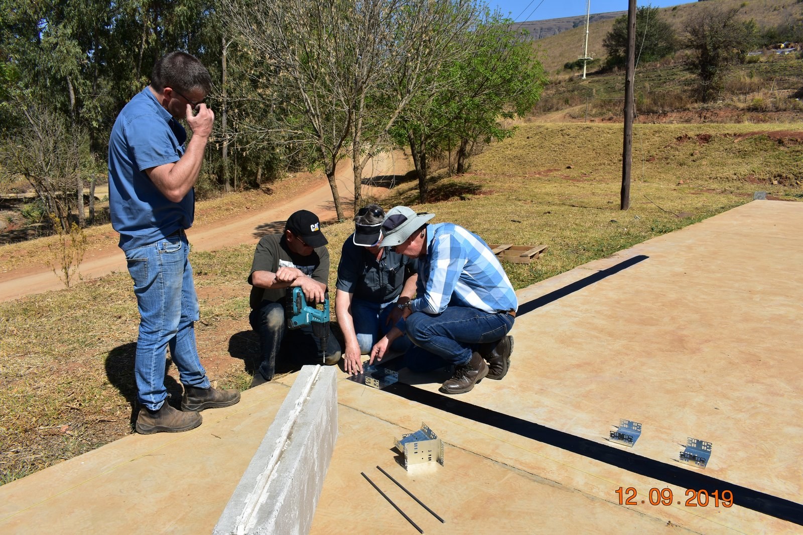 Crew drilling fixing brackets into a slab edge alongside a precast panel and embedded insulation strip.