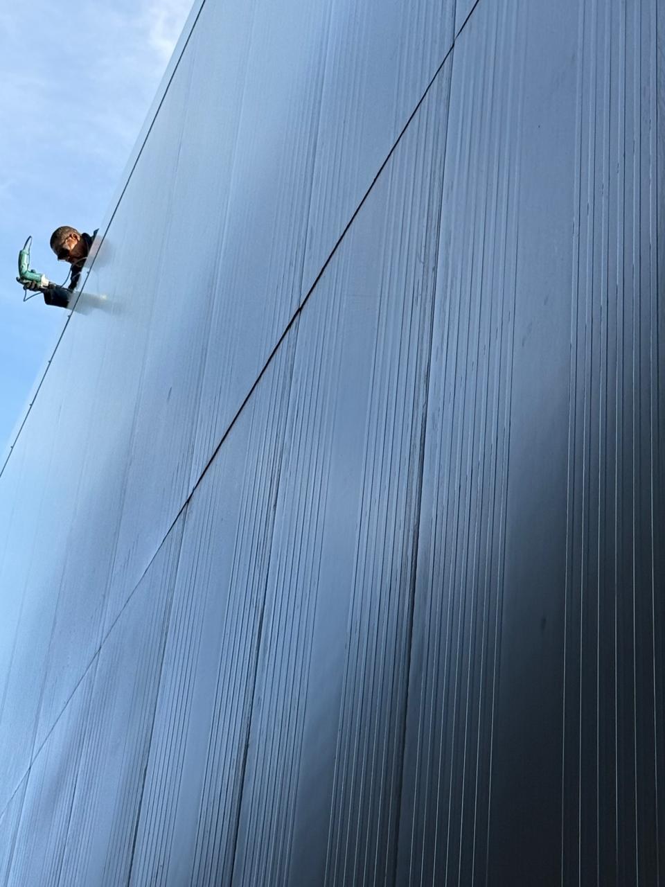 Looking up the finished panel elevation: the micro-ribbed face and the straight vertical panel joints, with an installer working the top edge with a cordless driver.