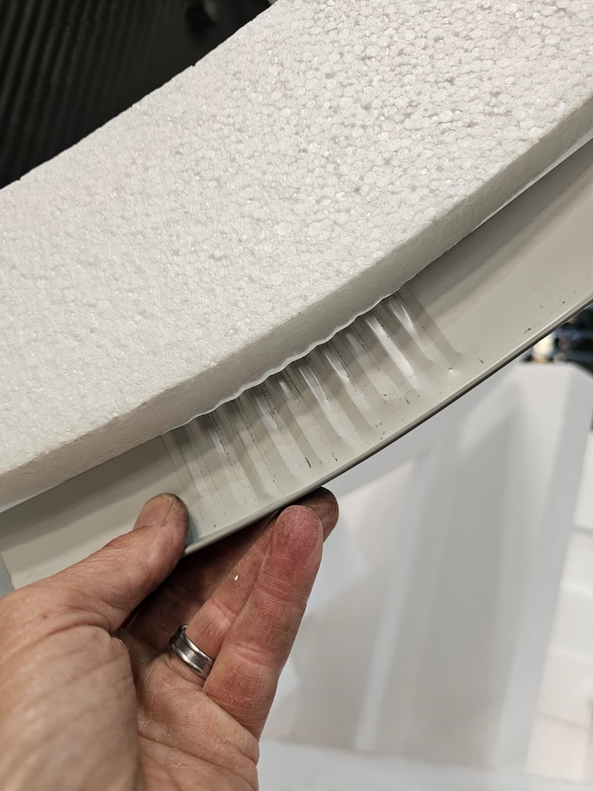 Panel corner held in the hand with the steel facing sheet lifted clear of the core, showing the white EPS bead foam behind the thin pressed-steel skin.