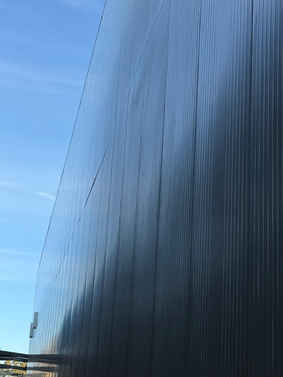 The completed panel wall raking away against the sky - continuous micro-ribbed faces with tight straight joints between adjoining panels.
