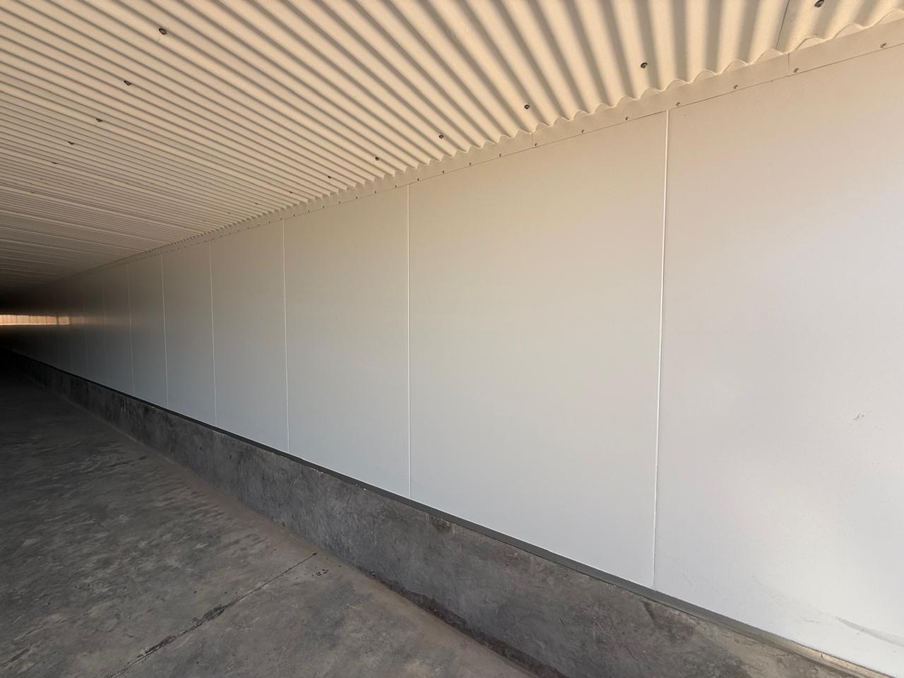 Inside the house: LiteSpan wall panels lining the sidewall, seated on the concrete plinth that lifts the panel clear of the wash-down zone. The roof sheeting overhead is still bare.