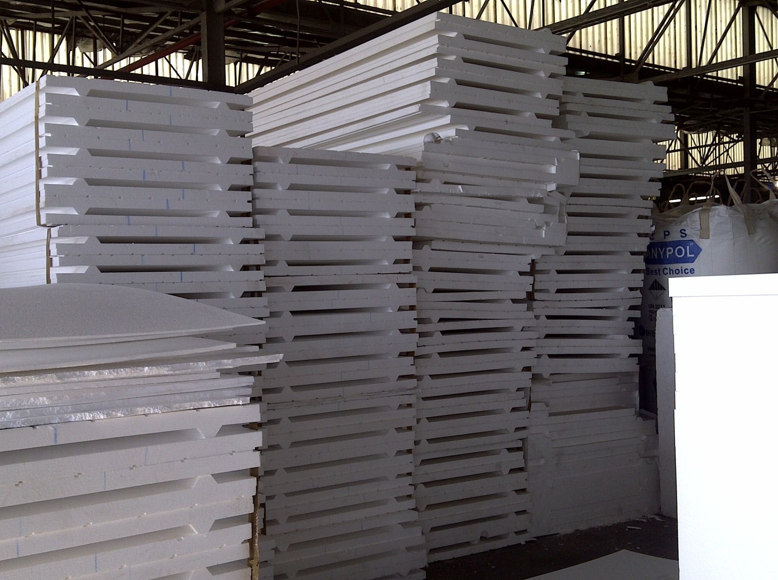 Panels stacked in the factory warehouse, with a raw EPS bead bag marked 'Anypol' in the background