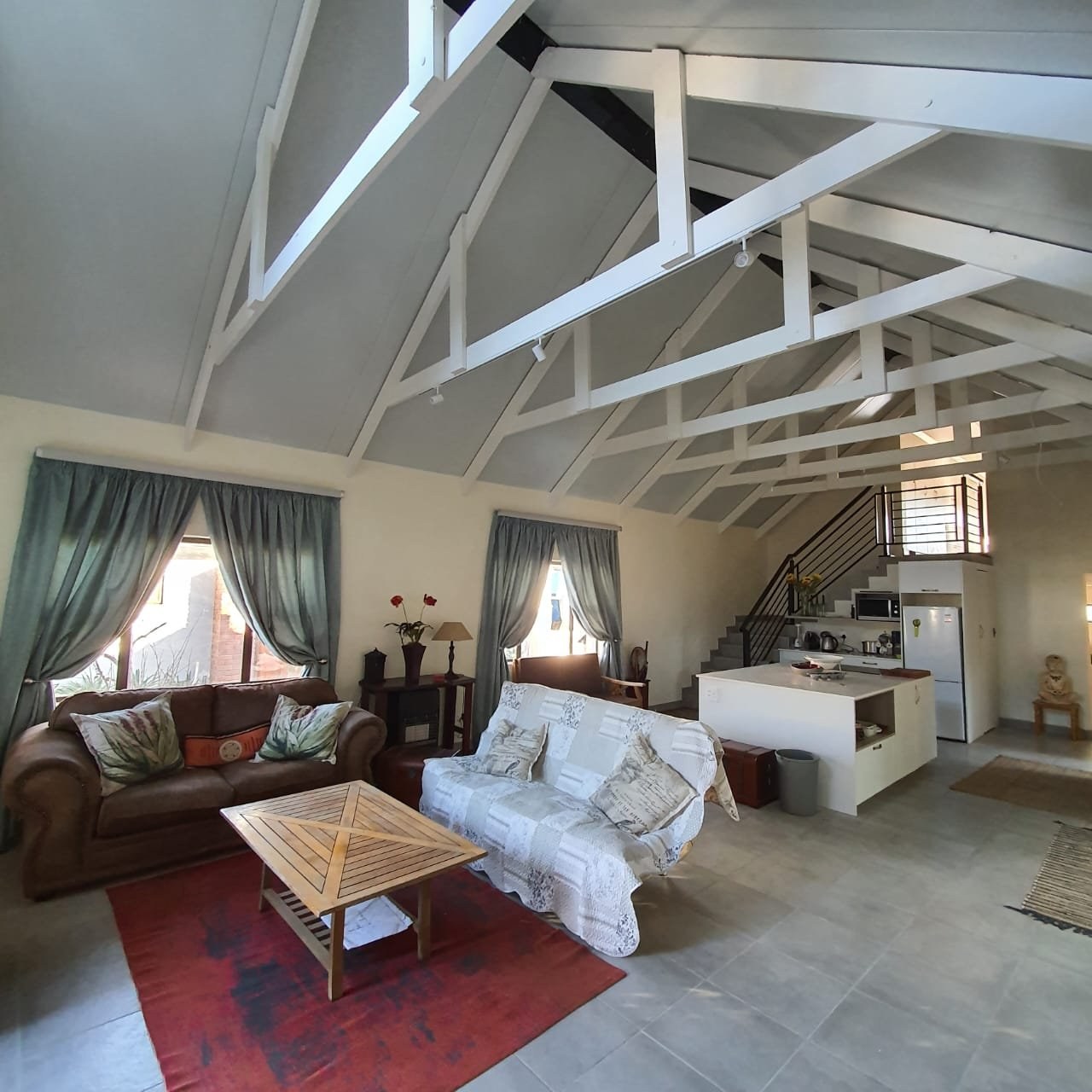 Panel ceiling in a vaulted open-plan living and kitchen area, with painted white roof trusses