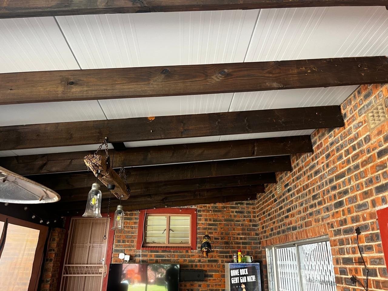 Panel ceiling installed under a patio roof alongside exposed wood beams