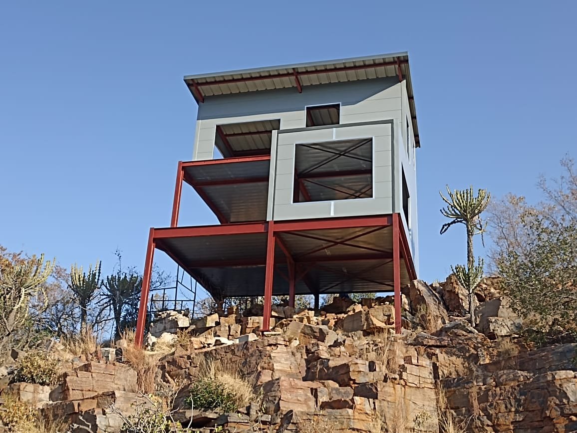 Small house on steel stilts with wall panels, built on a rocky outcrop