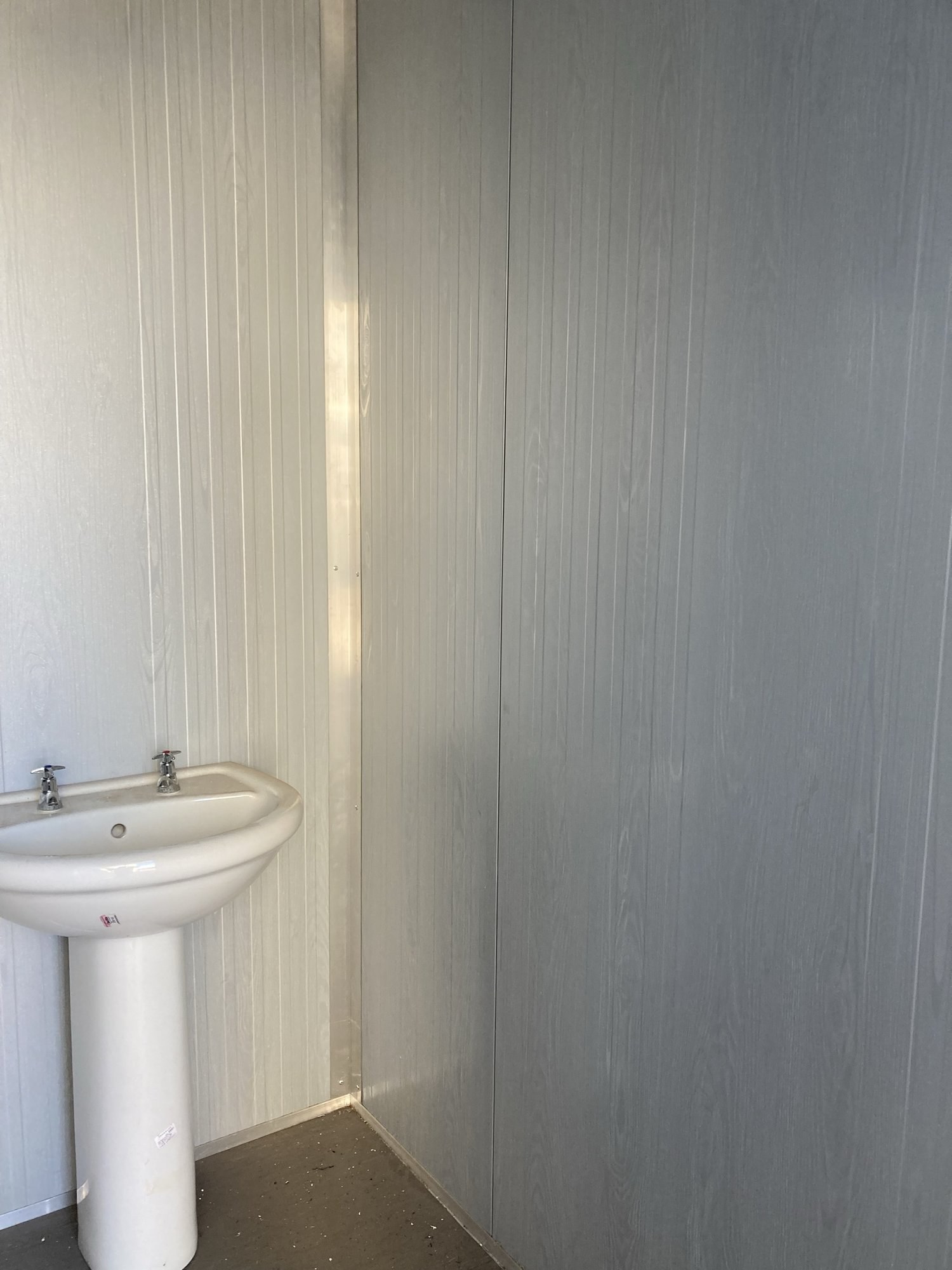 Interior corner of a panel-built cabin, wood-grain finish wall panels meeting above a pedestal basin