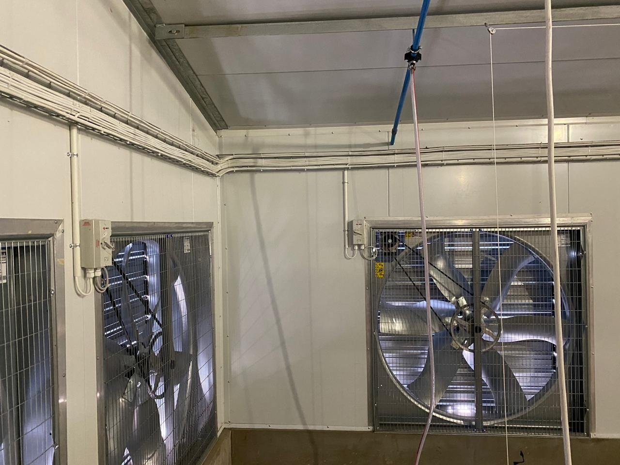 Extraction fan housing mounted through an exterior wall panel, farmland in the background