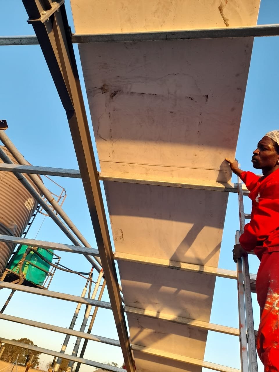 Installer fitting a wall panel on scaffolding beside a feed silo