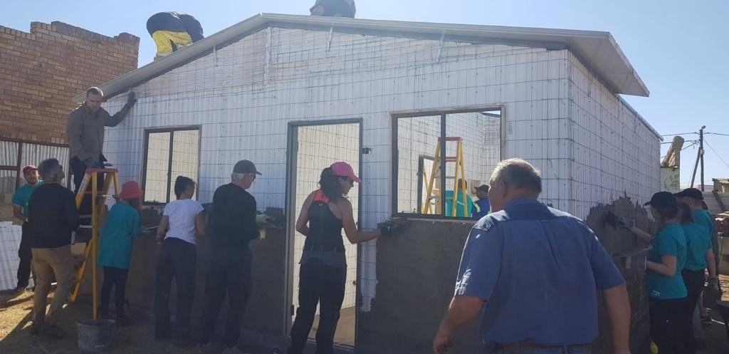 Team plastering the exterior of a panel-built house during a community build