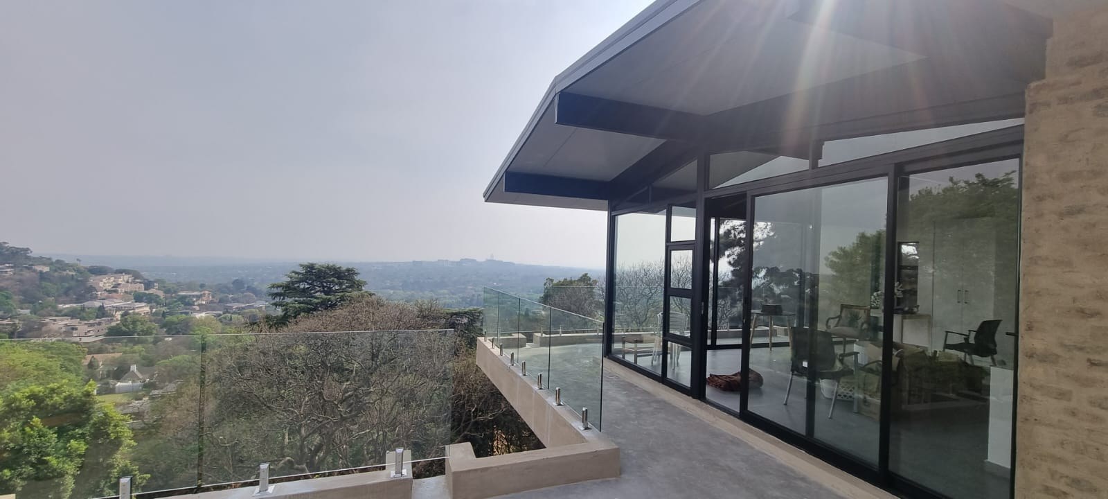Completed house: the roof cantilevers past the black-framed sliding glass and finishes in a slim closed edge, its flat pale underside running on as the soffit - one lay doing roof and ceiling. No rib profile or panel joint is visible from this angle.