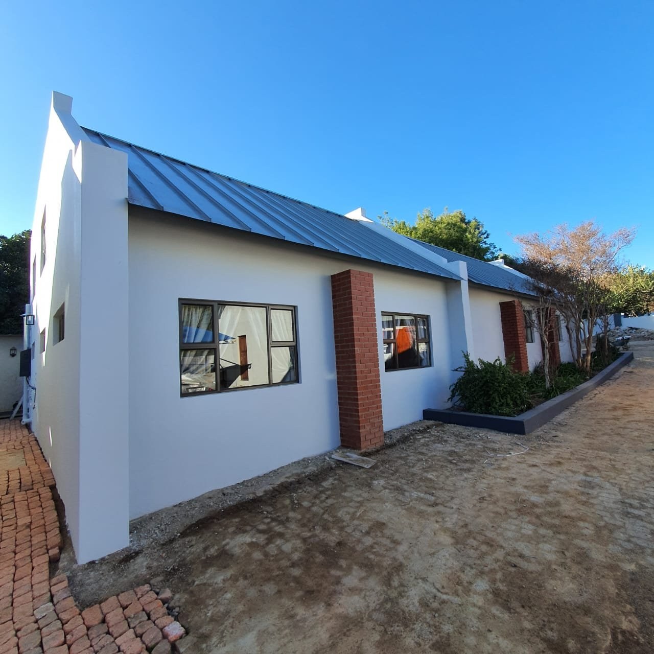 Completed house with a dark grey standing-seam LiteSpan roof over a gable-end wall and face-brick pillars