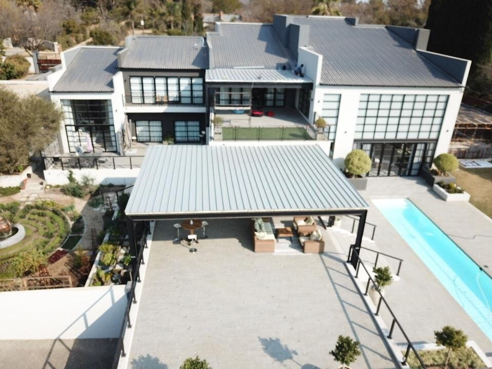 Aerial view of a large house with a completed standing-seam canopy roof over a pool-side patio