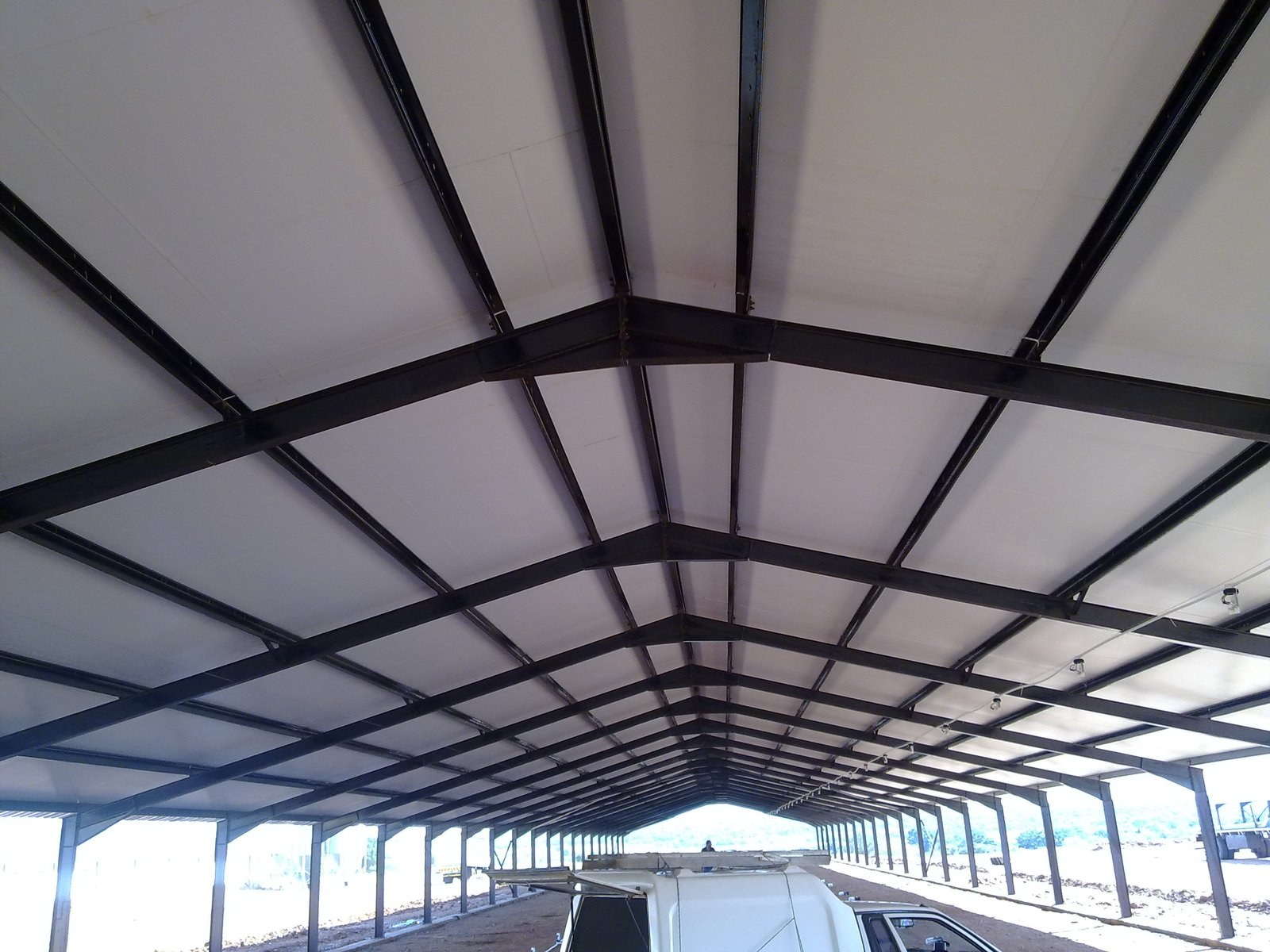 Underside view of insulated roof panels on steel purlins, with a bakkie parked beneath