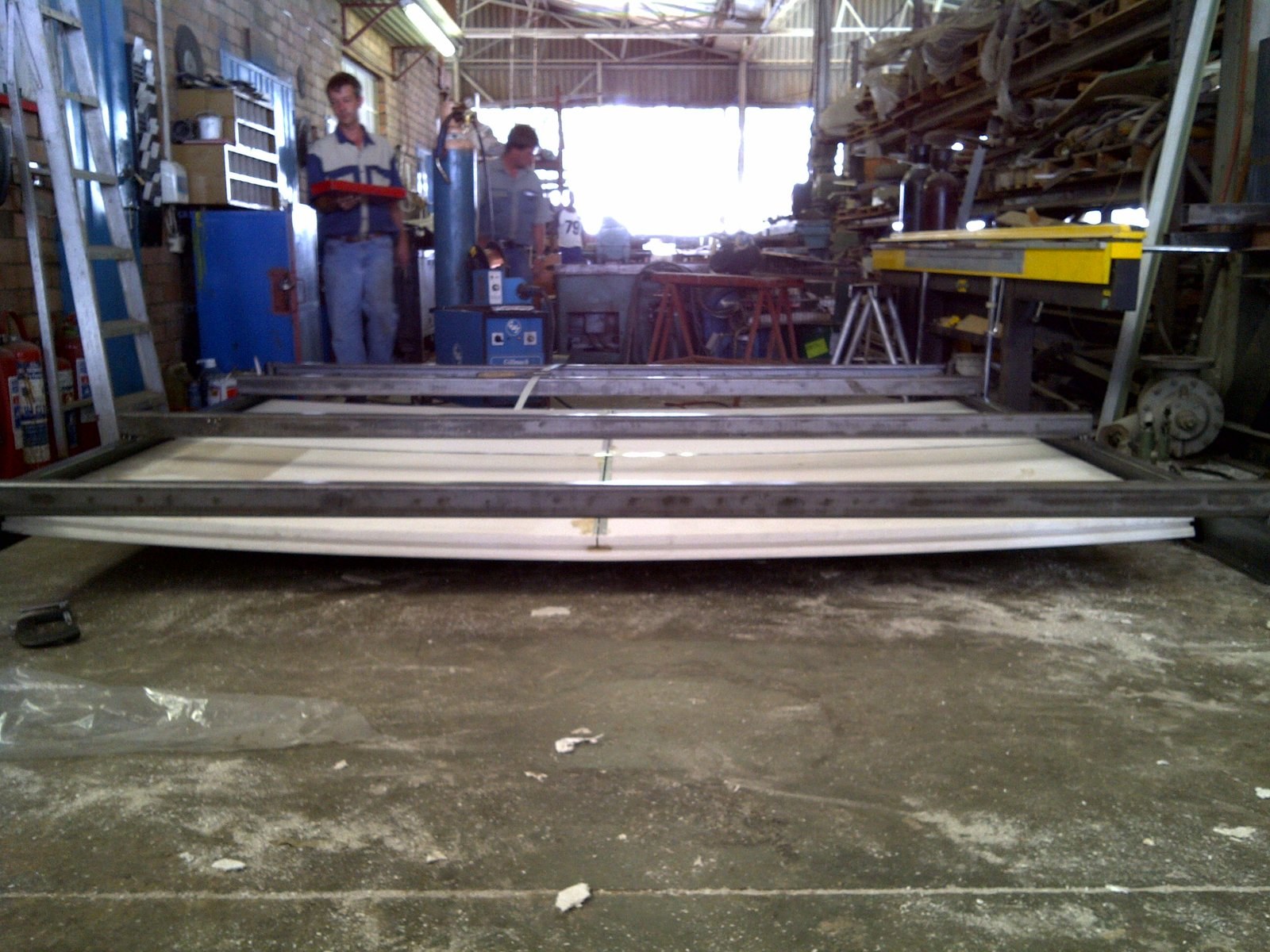 Curved roof panel being formed on a factory jig, workshop staff looking on
