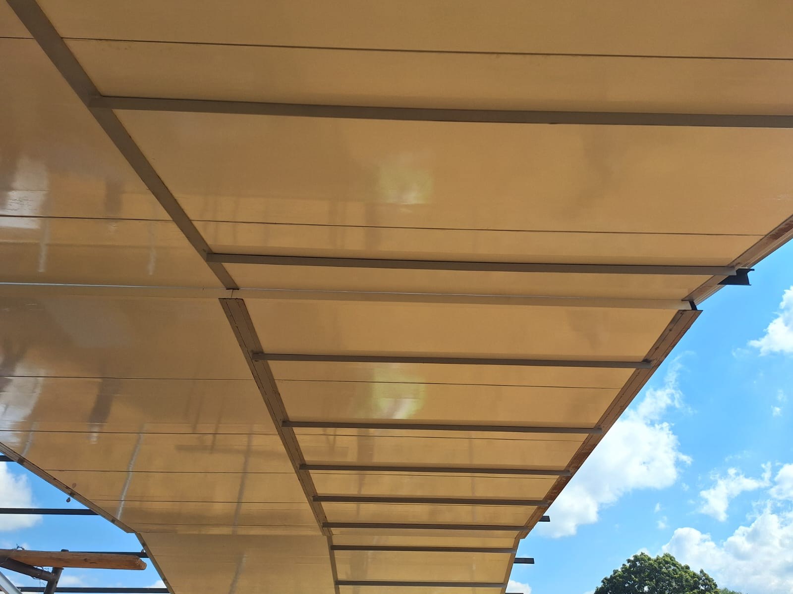 Underside of the cream faced panels seen from outside the building, fixed in bays between the purlins of the roof overhang.