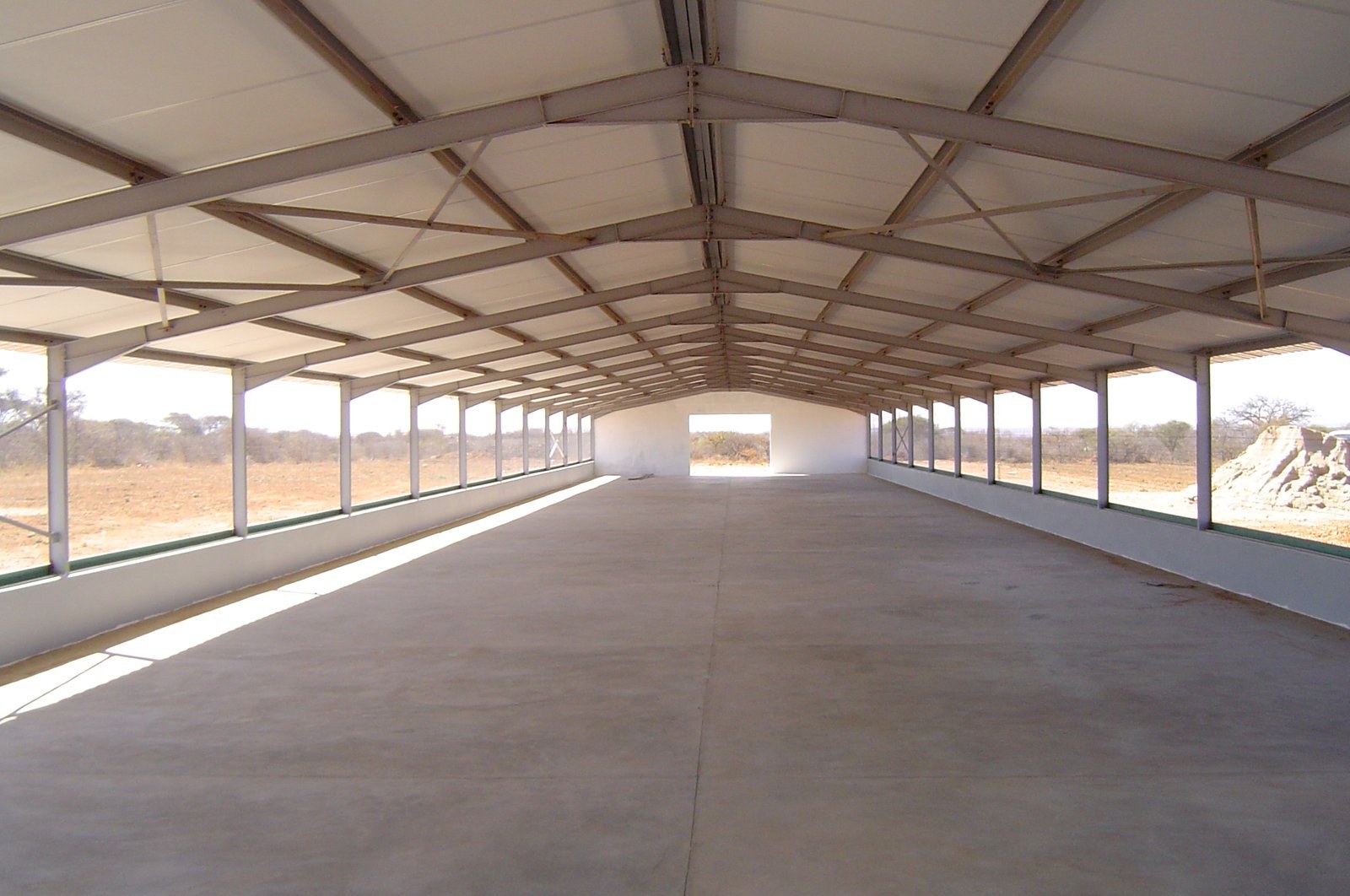 Completed open-sided shed with insulated roof panels over brick knee walls, veld setting
