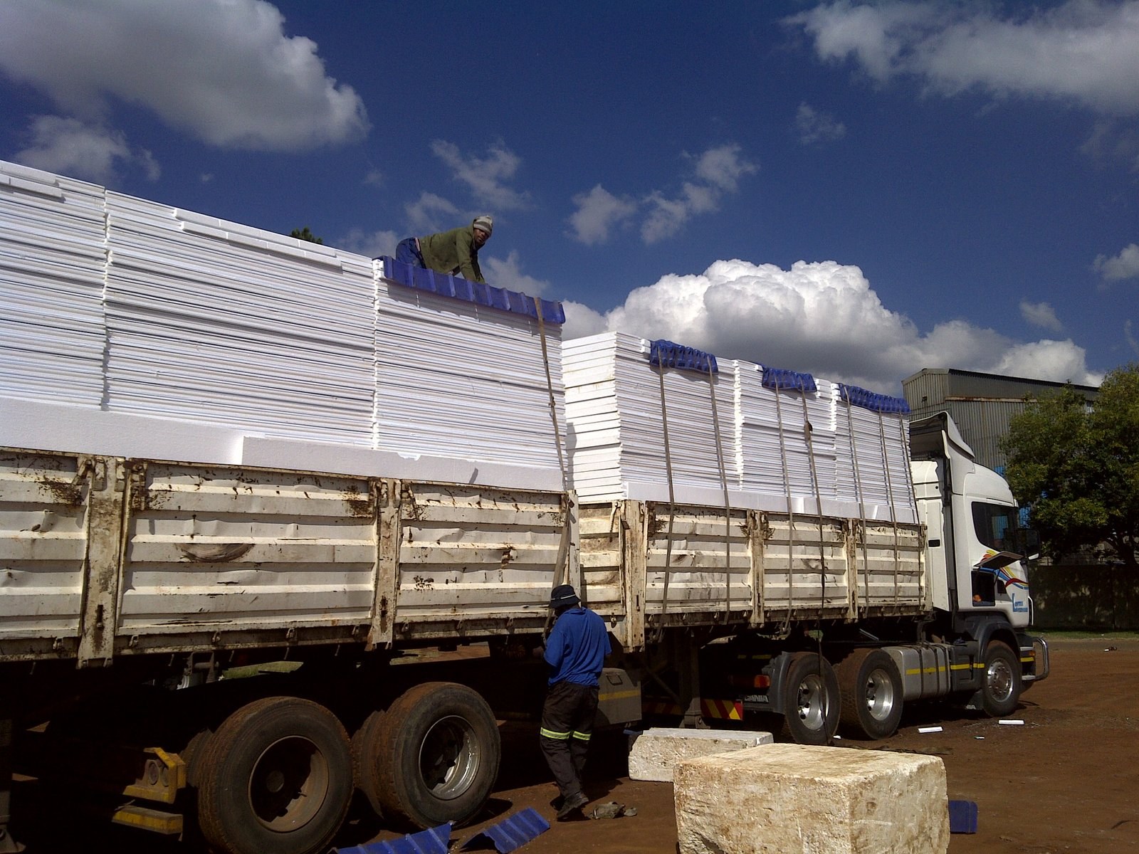 Workers strapping insulated roof panels onto a flatbed delivery truck