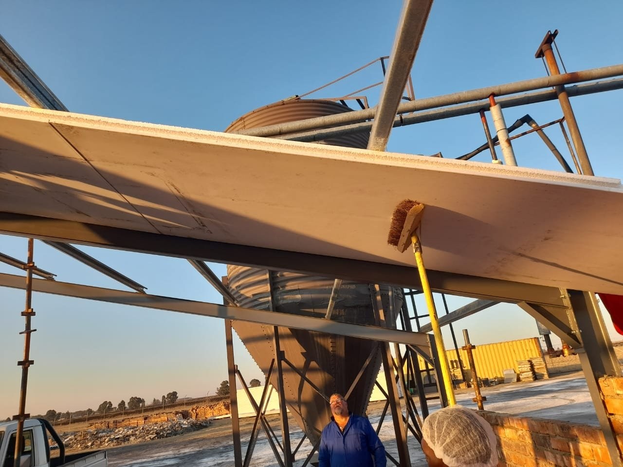 Worker brushing down the edge of a roof panel installed over a feed silo