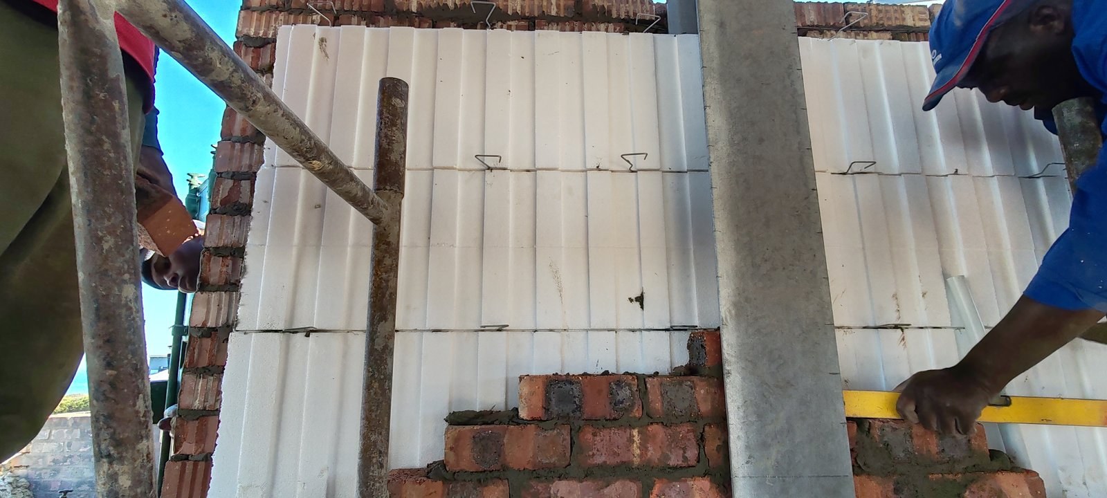 Checking brick level against a cavity board wall next to a steel column