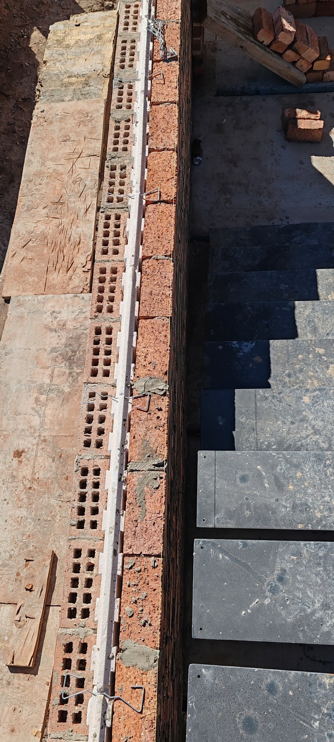 Overhead view along a brick and cavity board wall, paving slabs stacked below