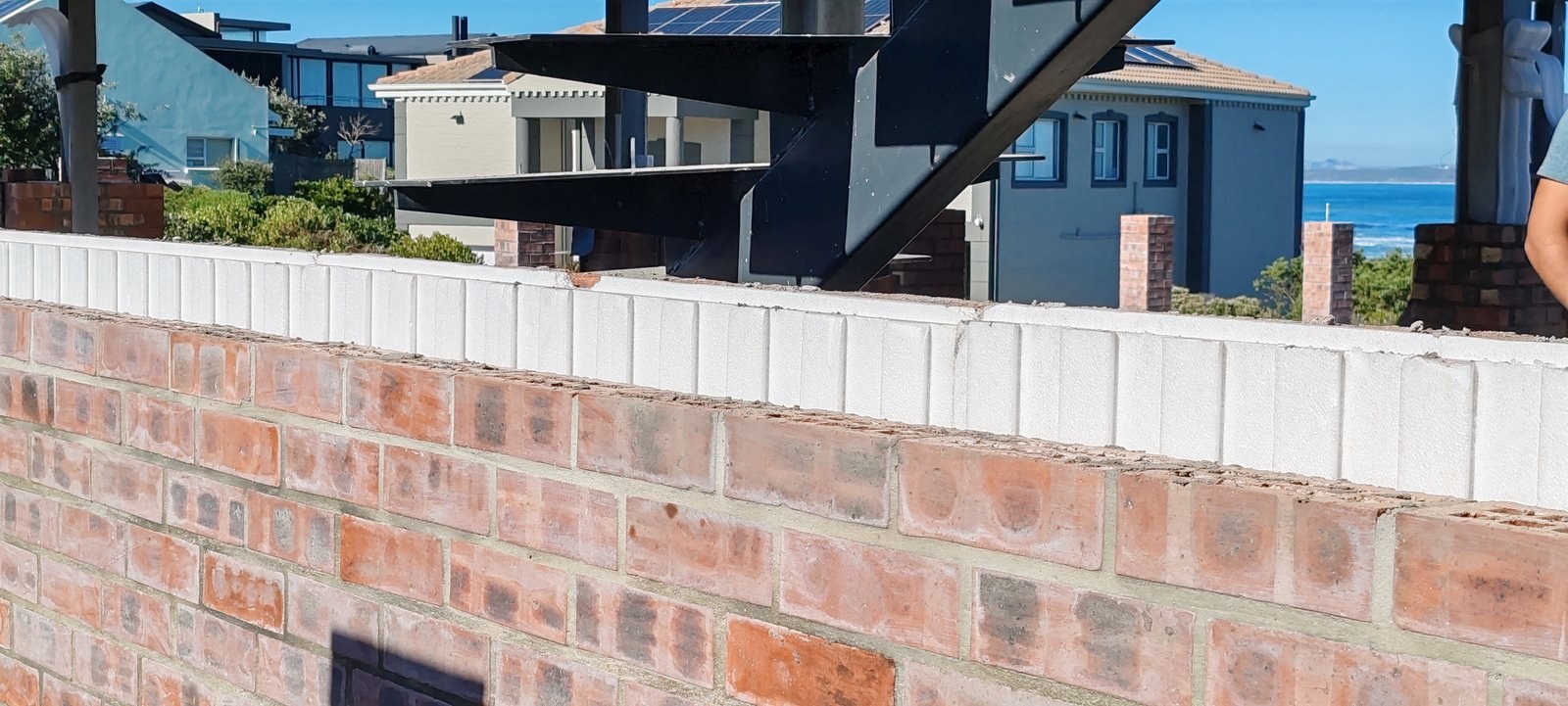 Insulated brick parapet wall under a steel roof structure, coastal houses in background