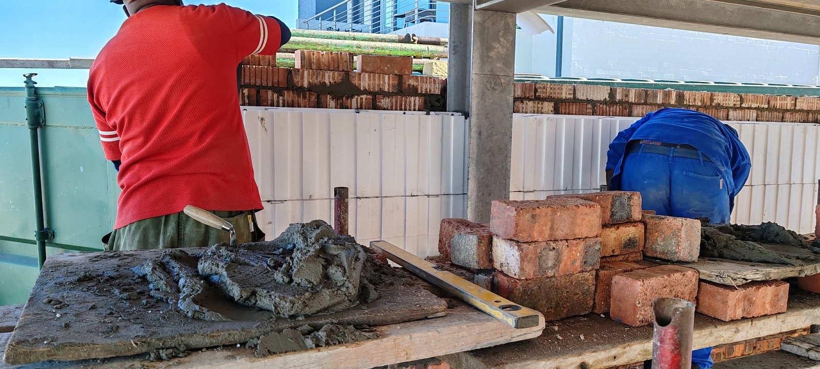 Two masons laying brick over cavity board at a mortar bench