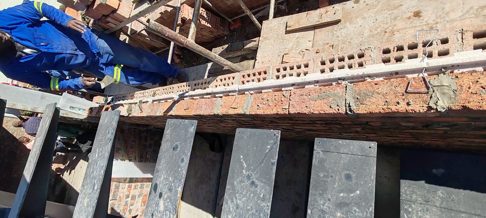 Worker walking along the top of an unfinished cavity board wall, paving slabs stacked below