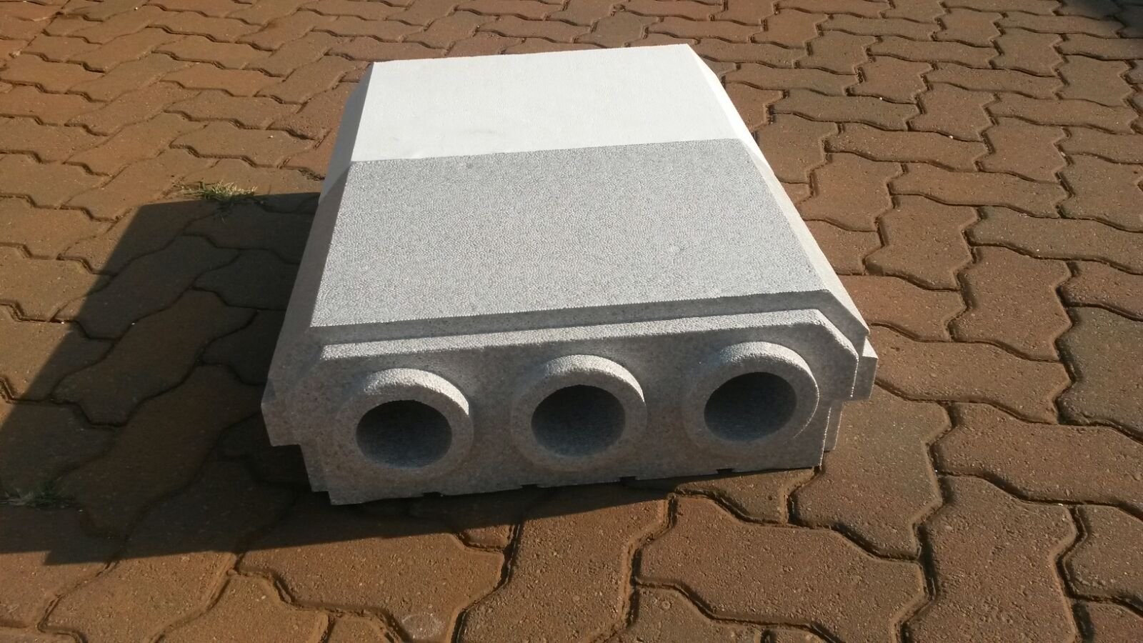 A single moulded EPS block photographed outdoors on paving, with the three circular cores running through it and the stepped rebates along its bottom edges clearly visible.